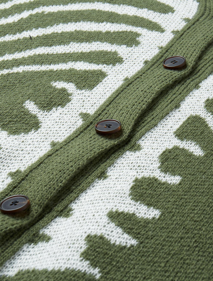 Close-up of a knitted cardigan with an olive green and white abstract pattern, featuring three dark brown buttons on a white background.