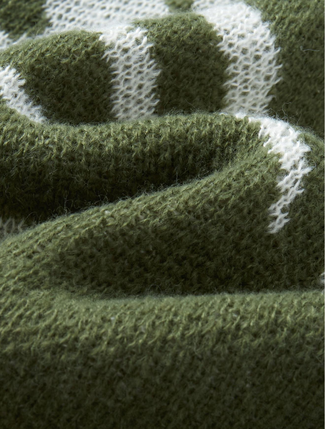 Close-up of a knitted textile in olive green with white knit patterning, showing the texture and weave detail.