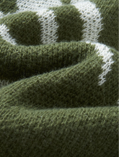 Close-up of a knitted textile in olive green with white knit patterning, showing the texture and weave detail.